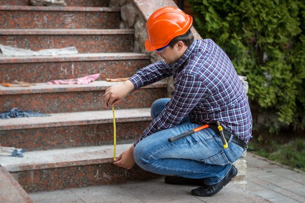 Young builder checking stairs height by measuring tape