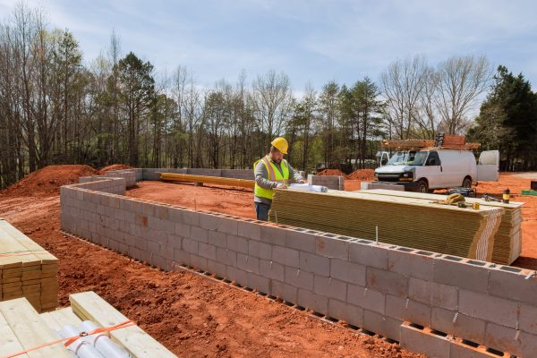 On construction site there is supervisor wearing hard hat safety vest checking construction plan for house project